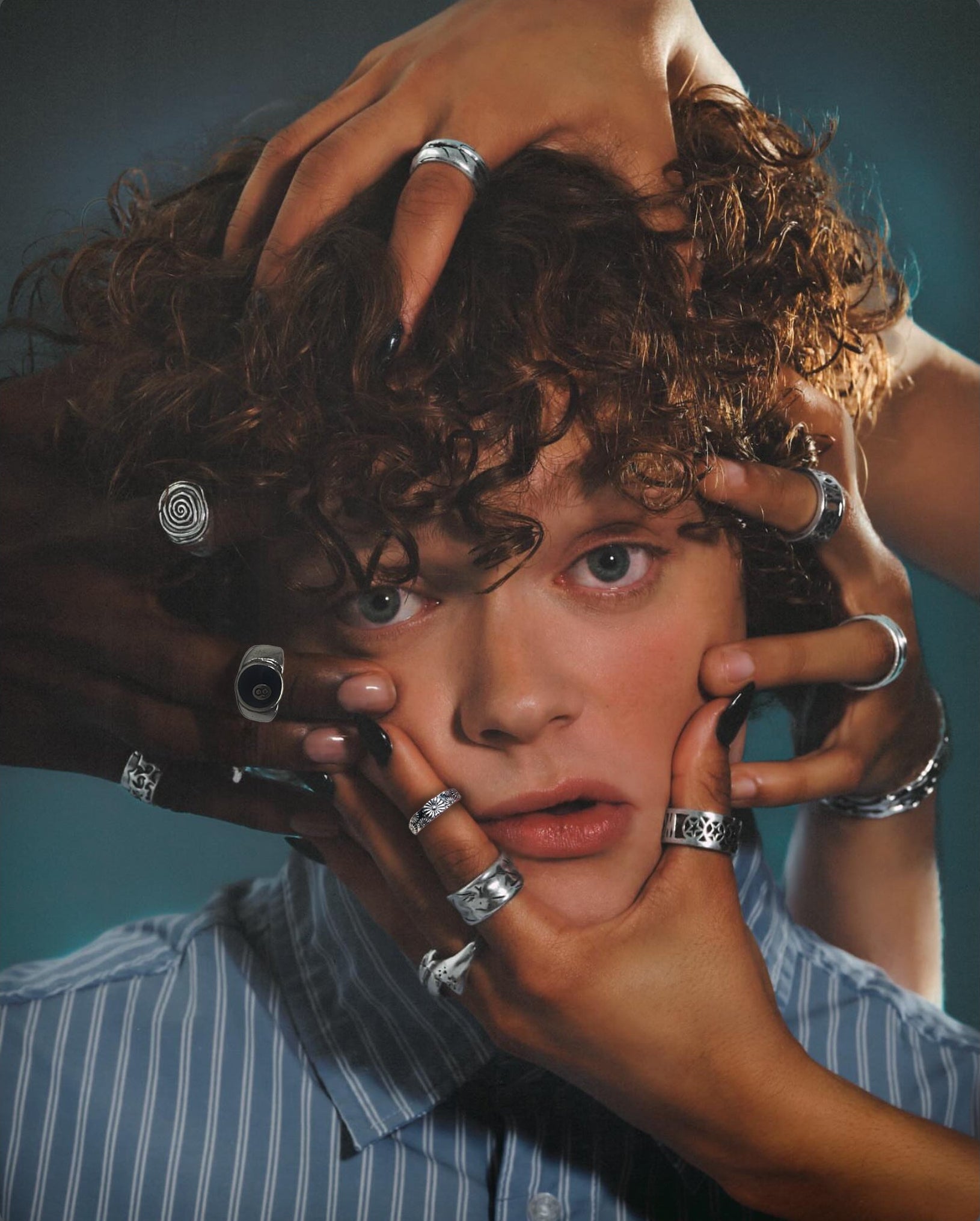 Hands wearing stacked silver rings framing a curly-haired model's face