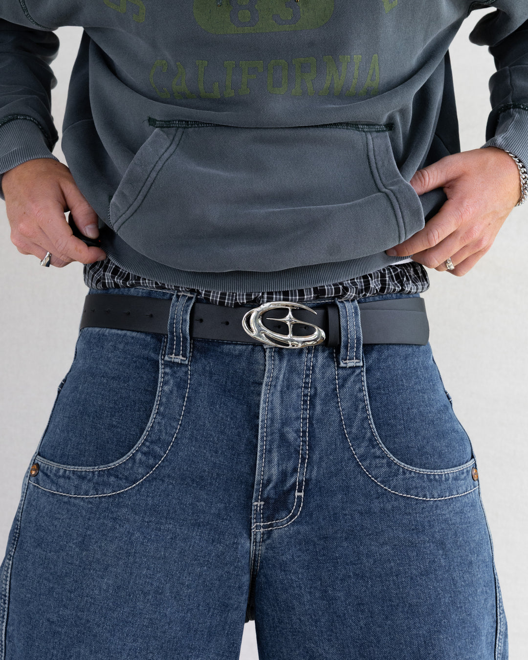 Rynor Orbit Chrome Buckle Belt – black leather belt with sculpted chrome crest buckle, worn by a model