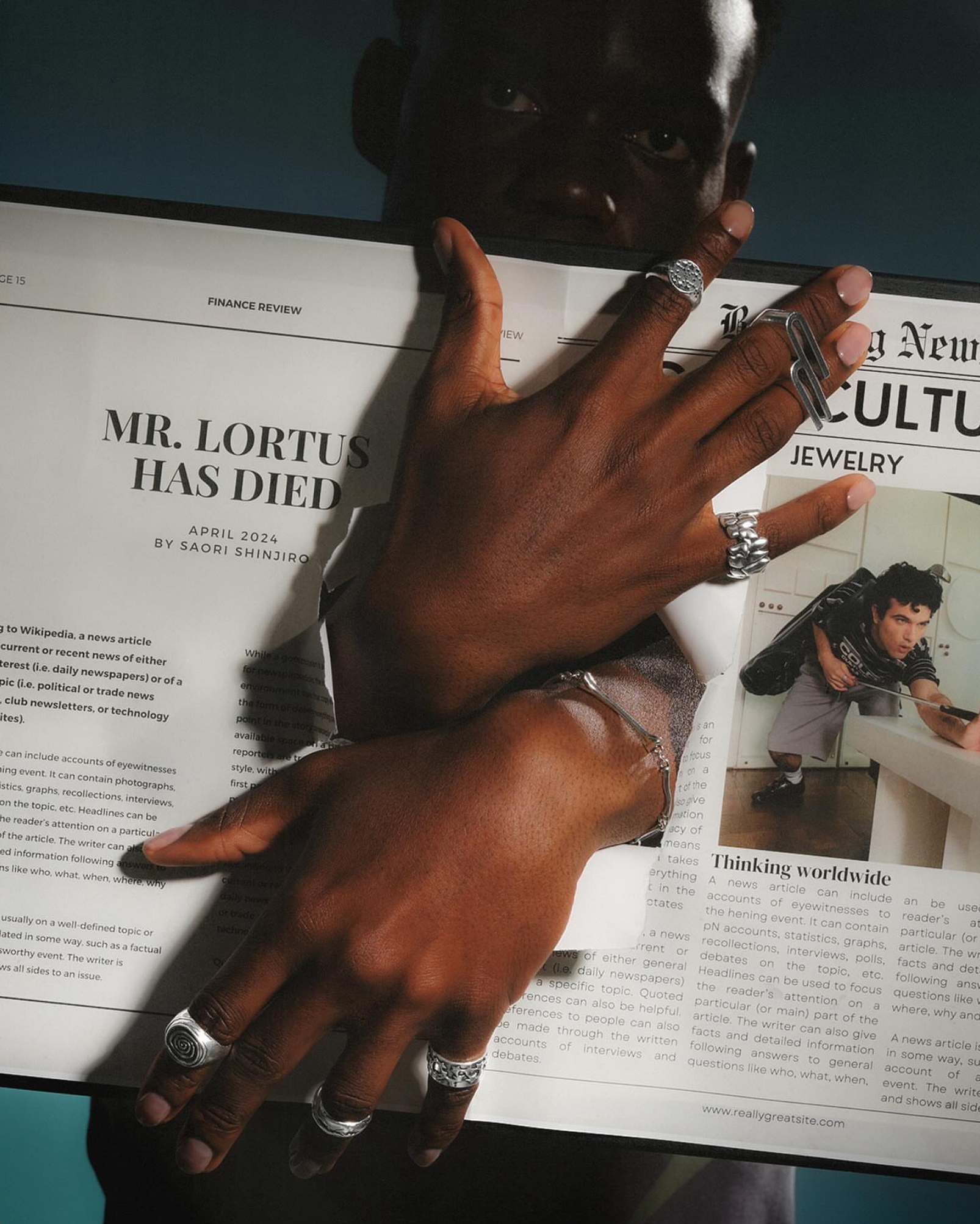 Hands wearing silver rings and a chain bracelet over a newspaper